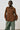 Person wearing a brown suede shirt and green pants against a white background