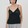 A model wearing a black lace camisole top with thin straps and light manta cargo pants