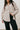 Person wearing a beige jacket over a black top and pants against a white background