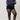 Person wearing a dark blue sweater, black shorts, and black tights against a plain background