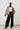 model wearing a camel jacket, white shirt, and black pants on a plain background