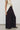 A model is shown from the side wearing a cream sleeveless vest and dark plum wide-leg trousers, paired with brown shoes, against a plain light gray studio background.