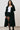 Woman wearing a black coat over a white top and black shorts on a plain background