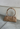 A beige vegan suede bowler bag with a classic silhouette, displayed against a textured background.
