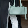 Person holding a light green handbag with a blurred background