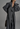 Person wearing a long dark gray trench coat against a plain background